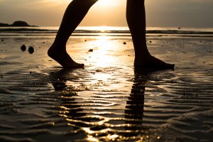 Feet of a young woman walking on the beach at sunset (backlit)