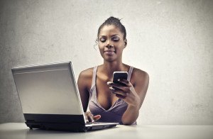 A beautiful black woman is smiling while is using a smart-phone