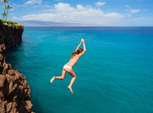 Woman jumping off cliff into the ocean. Summer fun lifestyle.