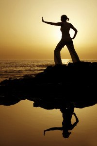 Yoga woman silhouetted against the setting sun with a natural reflection in a rockpool