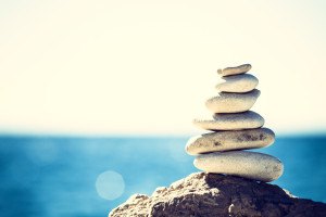 Stones balance vintage retro instagram like hierarchy stack over blue sea background. Spa or well-being freedom and stability concept on rocks.