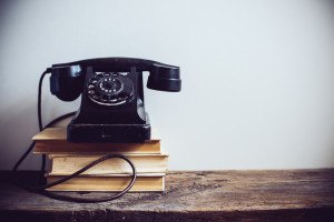 Black vintage rotary phone and books on rustic wooden table, on a white wall background