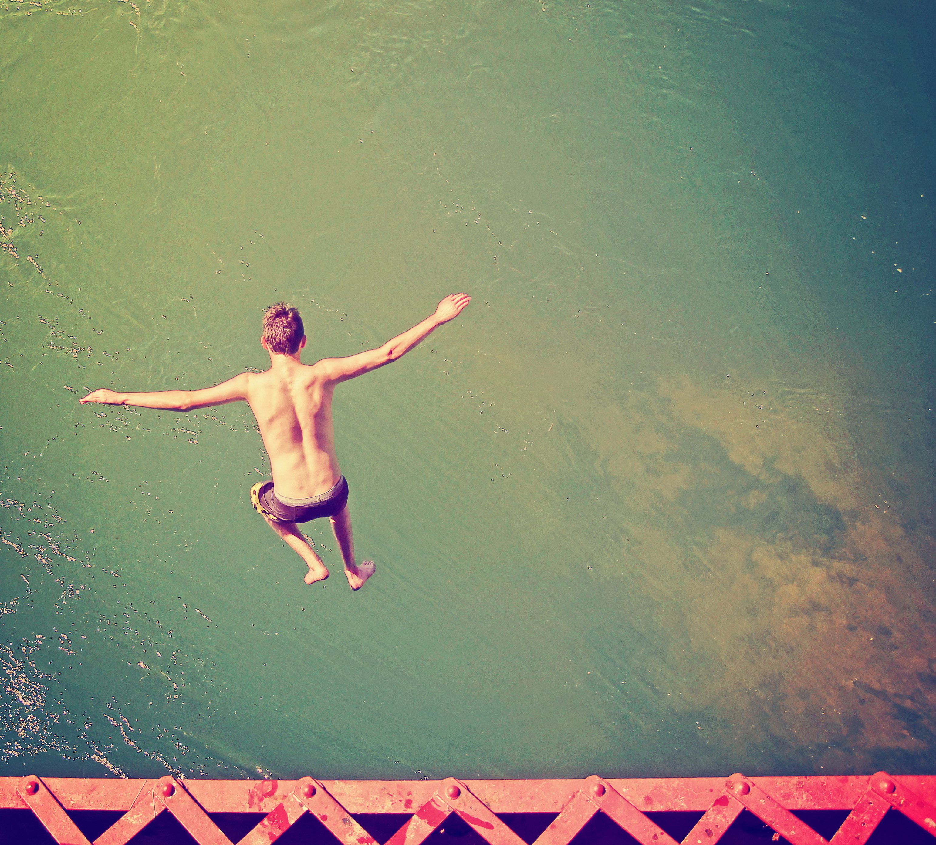 a boy jumping of an old train trestle bridge into a river done