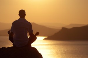 Guy meditating at sunset sitting on a rock by the sea