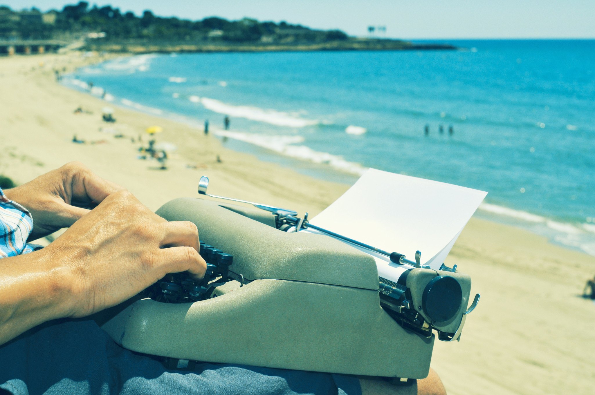 a young man typing in an old typewriter on the beach