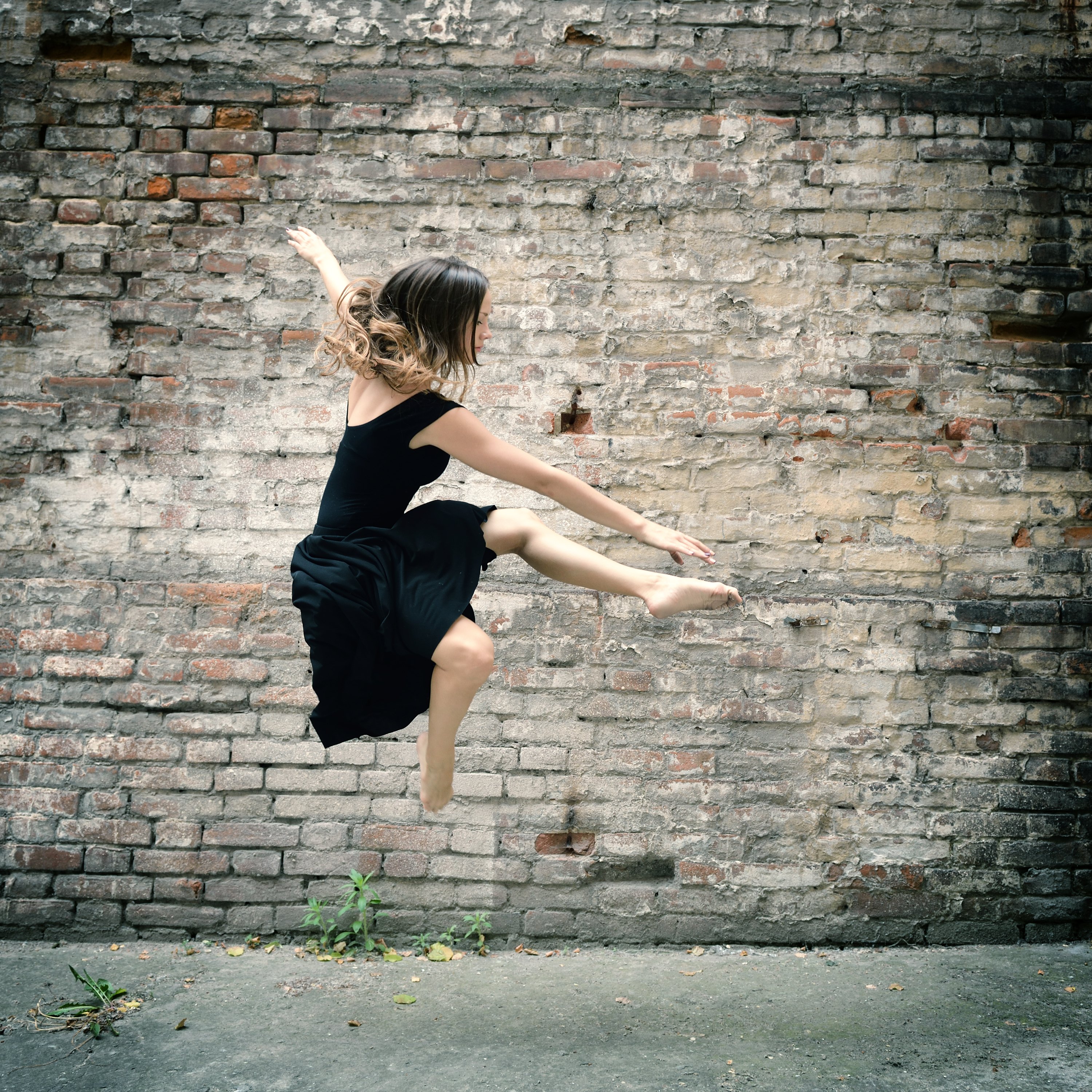 Attractive teen girl dancing outdoor against grunge bricks wall. Toned.