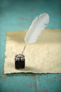 Inkwell and feather with old paper on grunge table