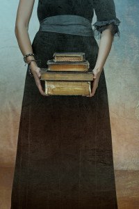 closeup of antique torn books with a hands of a young woman held against black dress on a grunge textured background